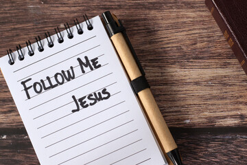 Follow Me, Jesus, handwritten quote in notebook with holy bible book on wooden background. Top...