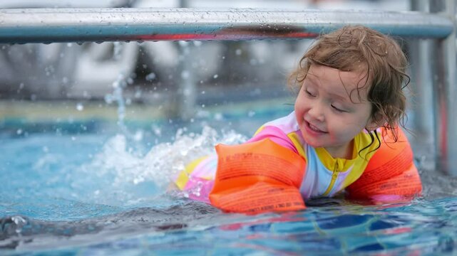 Girl paddles legs in water of pool while floaties keeping child safe