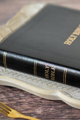 Holy bible book in rustic plate and golden fork on wooden table. Close-up. Christian fasting, spiritual food concept.