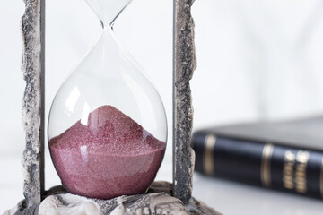 Close-up of hourglass and Christian holy bible book in the background. Copy space. Time countdown,...