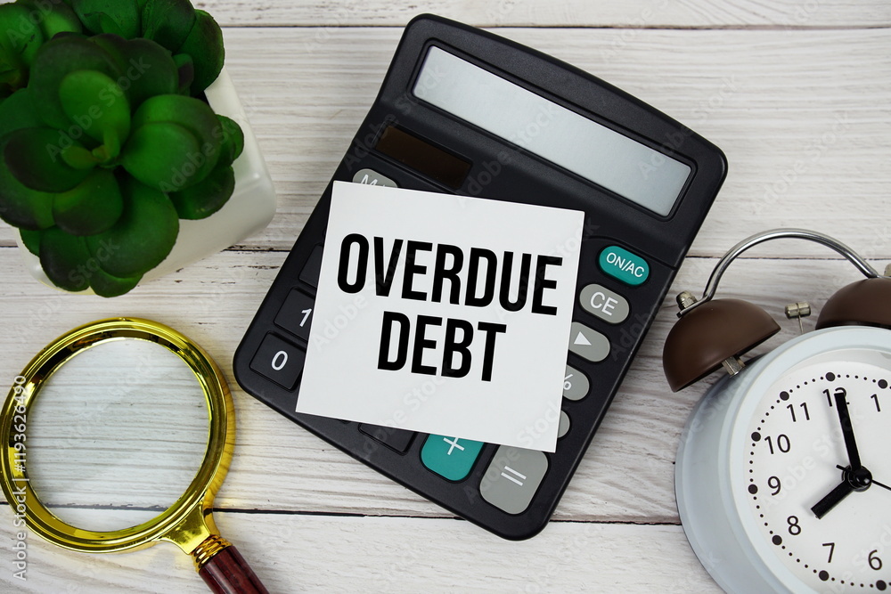 Poster overdue debt text message on sticky note with magnifying glass, alarm clock and calculator on wooden