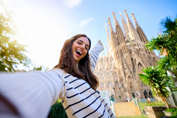 Young funny caucasian women taking a selfie in front of Sagrada Familia in Barcelona. Smiling beautiful girl on street of European city enjoying vacation happy and smiling. Funny tourism people