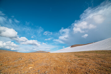 Orange tent on stony mountain pass in bright sun. Glacier on stone hillside under clouds in blue...