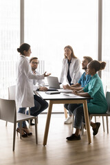 Vertical shot young healthcare medical workers discussing patient case in meeting room, listen speech, opinion, share experience Indian female in white lab coat. Collaboration between hospital staff