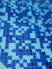 Raindrops falling into the swimming pool with blue tiles.