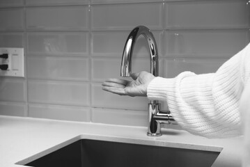 woman holding hand under kitchen faucet