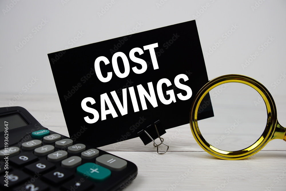 Poster cost savings text message on sticky note with magnifying glass and calculator on wooden