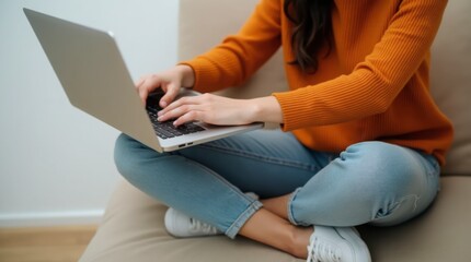Naklejka premium a person wearing an orange ribbed sweater working on a laptop. The person's hands are on the keyboard, of the laptop.