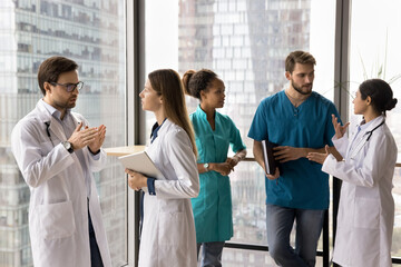 Group of multiethnic doctors standing in pairs in clinic hallway, engaged professional discussion...