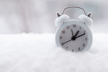 White alarm clock on snow in nature. Close-up. Copy space. Winter time change concept.