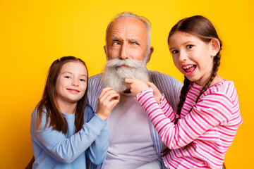 Grandfather Enjoying Playful Time With Two Young Granddaughters Smiling in Bright Yellow Background