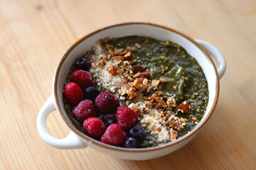 Beige bowl with green smoothie, frozen berries and homemade granola, served on the table. Selective focus.