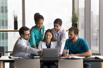 Five multiethnic clinic staff members, professional medical workers working together using laptop,...