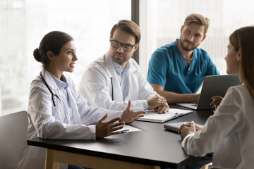 Diverse doctors engaged in meeting led by Indian GP, discuss complex patient cases, review medical history, diagnostic results, and treatment plans, take part in collaborative approach to patient care