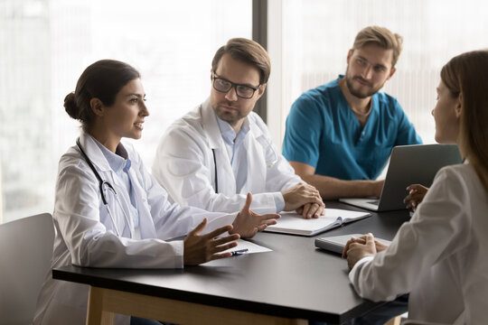 Diverse doctors engaged in meeting led by Indian GP, discuss complex patient cases, review medical history, diagnostic results, and treatment plans, take part in collaborative approach to patient care