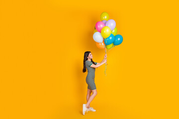 Young woman holding vibrant balloons against a bright yellow background, smiling and portraying happiness