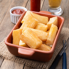 Traditional brazilian fried manioc in a plate with ketchup, pepper and beer over wooden table