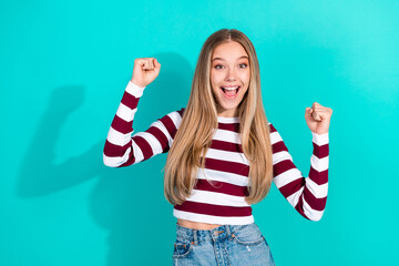 Excited young woman in a striped sweater celebrating victory with an enthusiastic gesture against a...