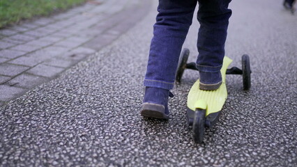 Child feet riding scooter. Baby toddler close-up foot rides scooter