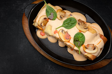 Pancakes with mushrooms, sauce and spinach, in a frying pan