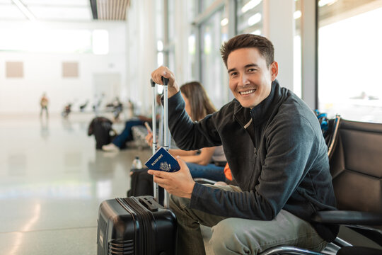 Happy smiling young male traveler holding USA passport at airport.	