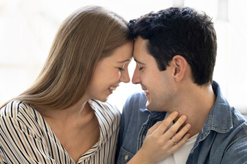 Happy sweet Latin couple hugging with closed eyes and heads touch, talking, smiling, laughing. Young husband and wife enjoying romantic moment, affection, close relationship