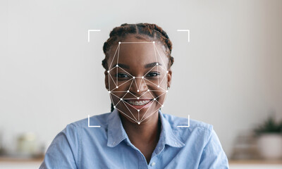 A cheerful individual with braided hair sits indoors, engaged in a facial recognition process. The...