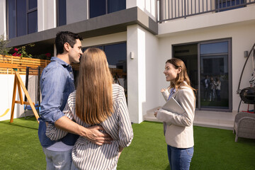 Happy real estate agent woman showing house for sale to young couple of customers, buyers, standing...