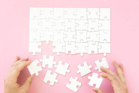 Hands collecting white blank jigsaw puzzle on pink background, top view