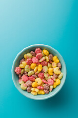 Colorful breakfast cereals in the shape of various fruit in bowl on blue background. Top view.