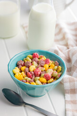 Colorful breakfast cereals in the shape of various fruit in bowl on white table.