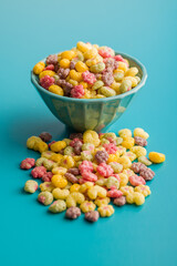 Colorful breakfast cereals in the shape of various fruit in bowl on blue background.