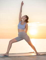 Sporty woman practicing yoga outside, doing relaxing stretching workout for body flexibility on seashore at sunrise outdoors