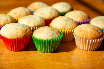 Mini banana muffins sit on a wooden kitchen table with various colors of muffin cups.