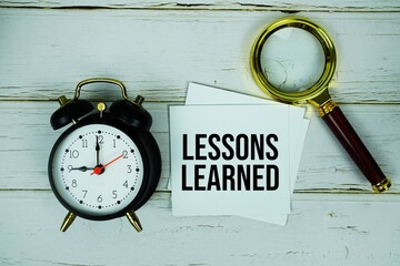Lessons Learned text message on sticky note with magnifying glass and alarm clock on wooden...
