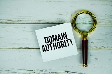 Domain Authority text message on sticky note with magnifying glass on wooden background