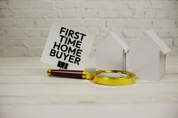 First Time Home Buyer text message on sticky note with magnifying glass and house model on wooden background