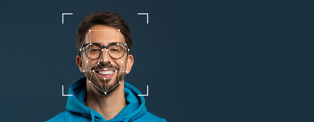 A smiling man wears glasses and a hoodie while facial recognition technology overlays a geometric pattern on his face. The background is a solid color, emphasizing facial identification.