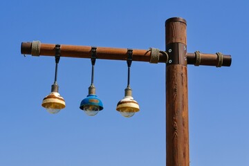 Wooden street lamppost with hanging three vintage weathered rusty lamp bulb lantern in trendy eco...