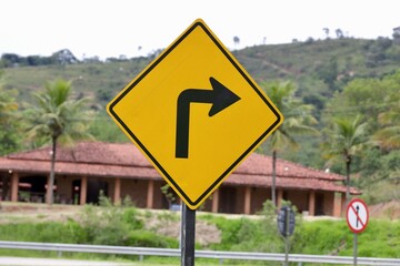 Placa de sinalização de transito vire a direita na cor amarela com fundo desfocado de uma casa.