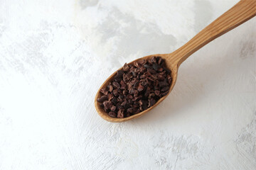 Cocoa nibs in wooden spoon on textured table, close-up. Sugar-free product, Natural antidepressant. Good chocolate chip alternative.
