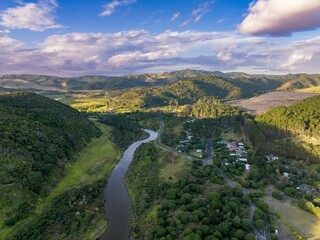 Aerial view of Bethells Beach town nestled in a valley, with a winding river and roads snaking...