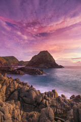 Rocky Coast Meets Ocean Waves Under a Purple Sunset Sky with Majestic Coastal Landscape Serenely