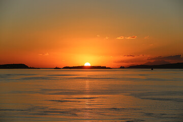 Greece. Fiery orange sun dips below the horizon over the sea and islands