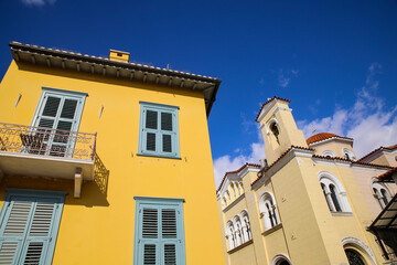 Athens, Greece. Yellow Mediterranean building with balconies and blue shutters and a red Greek church and dome