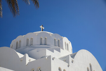 Thira, Santorini, Greece. Greek orthodox church, white washed, scalloped windows, cross and palm trees