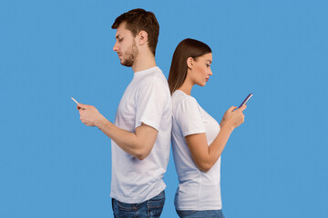 Smartphone Addiction. Serious man and woman standing back to back and using their smart phones,...