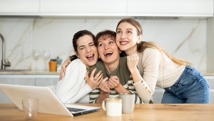 Joyful middle-aged women gloating over having won a prize sitting at notebook in the kitchen