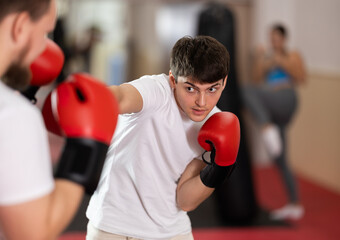 During training, young man wearing boxing gloves learns how to fight opponent. He punches, tries to...