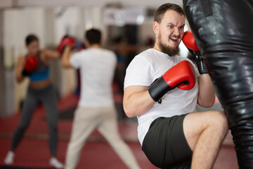Man making a knee kick on a punching bag at the martial arts section. European man in Muay Thai...